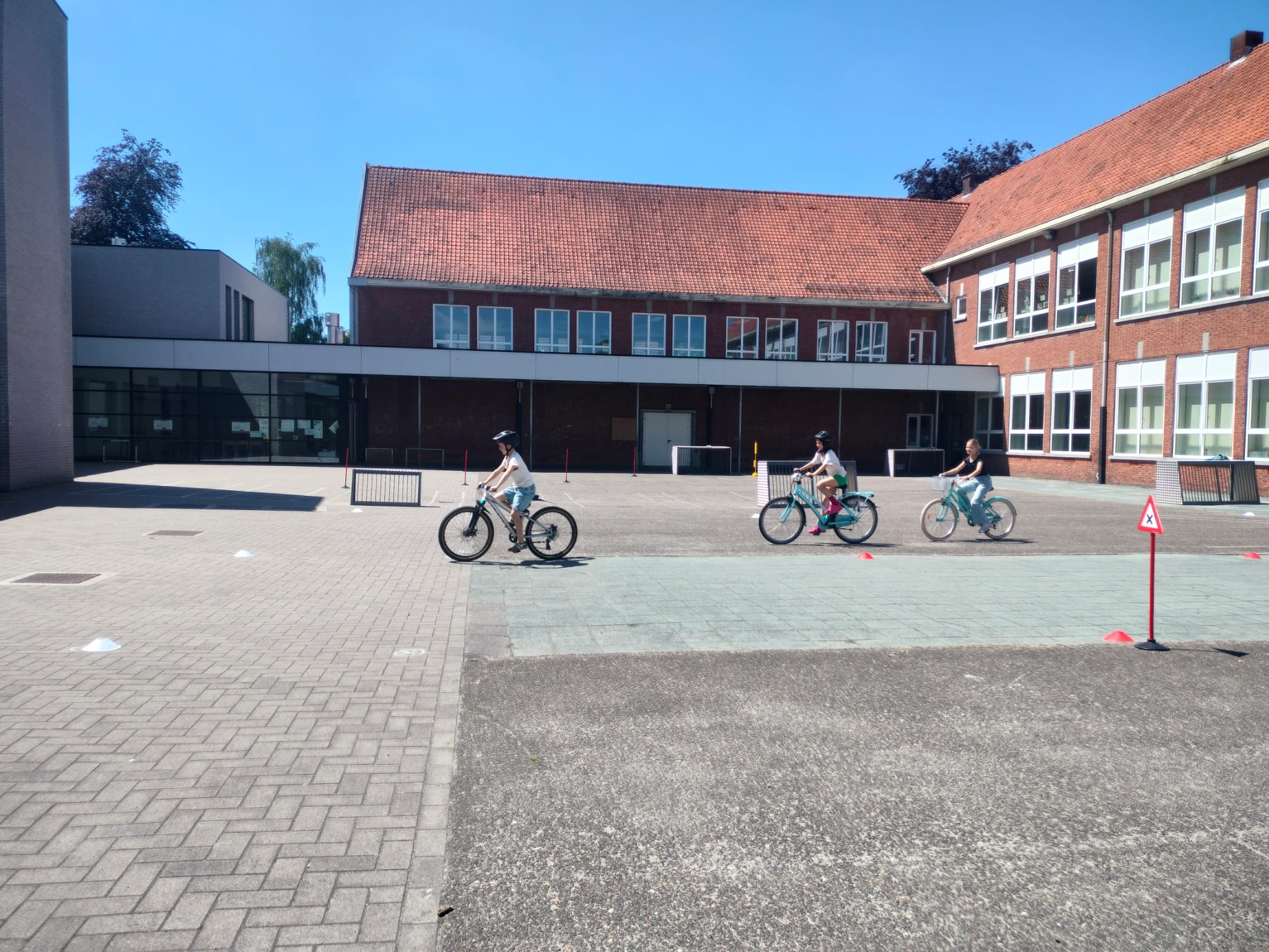 Drie kinderen fietsen op de speelplaats het fietsparcours af. 